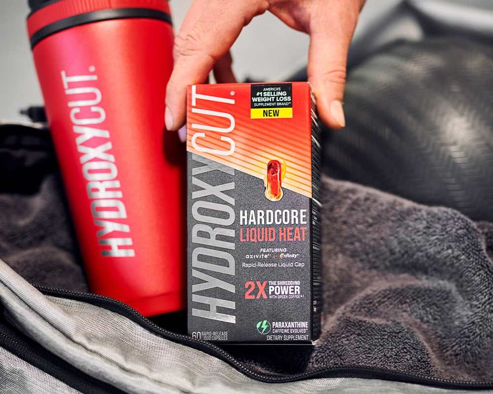 Hydroxycut original bottle on a counter with a glass of water and a woman holding two capsules